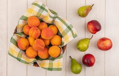 Canasta de duraznos junto con peras y manzanas regadas en la mesa para hacer recetas con fruta para niños