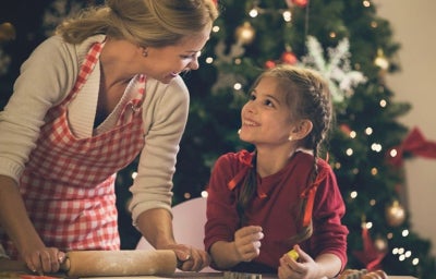 Madre e hija preparando galletas juntas mientras disfrutan el ambiente típico de las películas de Navidad.