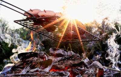 Parrilla metálica suspendida en fogón de leña, asándose sobre brasas ardientes.