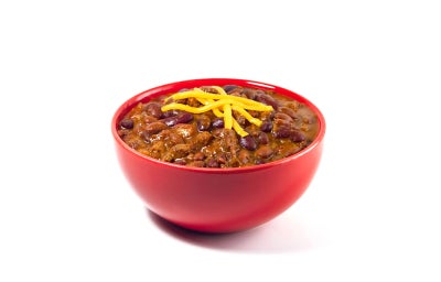 Tazón de chili con carne y queso rallado derretido sobre fondo rojo vibrante.