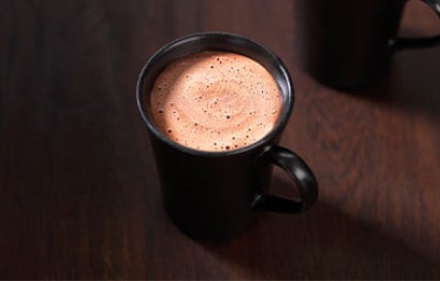 Dos tazas de chocolate caliente con espuma sobre superficie oscura, estilo artesanal.