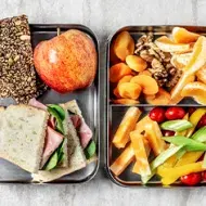 Comida para viaje: barras de cereal, sándwich, frutas, verduras picadas y frutos secos. 