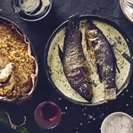 Dos bagres fritos en salsa en toma cenital sobre un fondo negro y acompañados de arroz amarillo