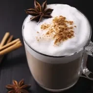 Bebida caliente con leche, canela y anís en una taza de vidrio grueso en una toma en picado