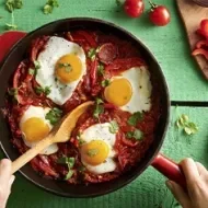 Huevos shakshuka con hierbas, salsa de tomate, pan y pimentón picado en toma cenital