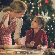 Madre e hija preparando galletas juntas mientras disfrutan el ambiente típico de las películas de Navidad.