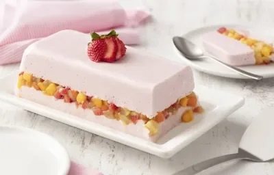 fondo blanco de madera con tela rosa claro, un plato blanco con una capa de gelatina con yogur de fresa, una capa de macedonia de frutas y otra capa de gelatina con yogur de fresa. fondo blanco de madera con tela rosa claro, un plato blanco con una capa de gelatina con yogur de fresa, una capa de macedonia de frutas y otra capa de gelatina con yogur de fresa.