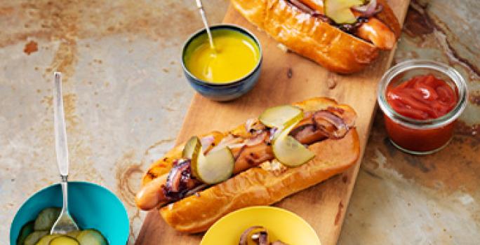 Tabla con hot dogs con salsas kétchup y mostaza Tabla con hot dogs con salsas kétchup y mostaza